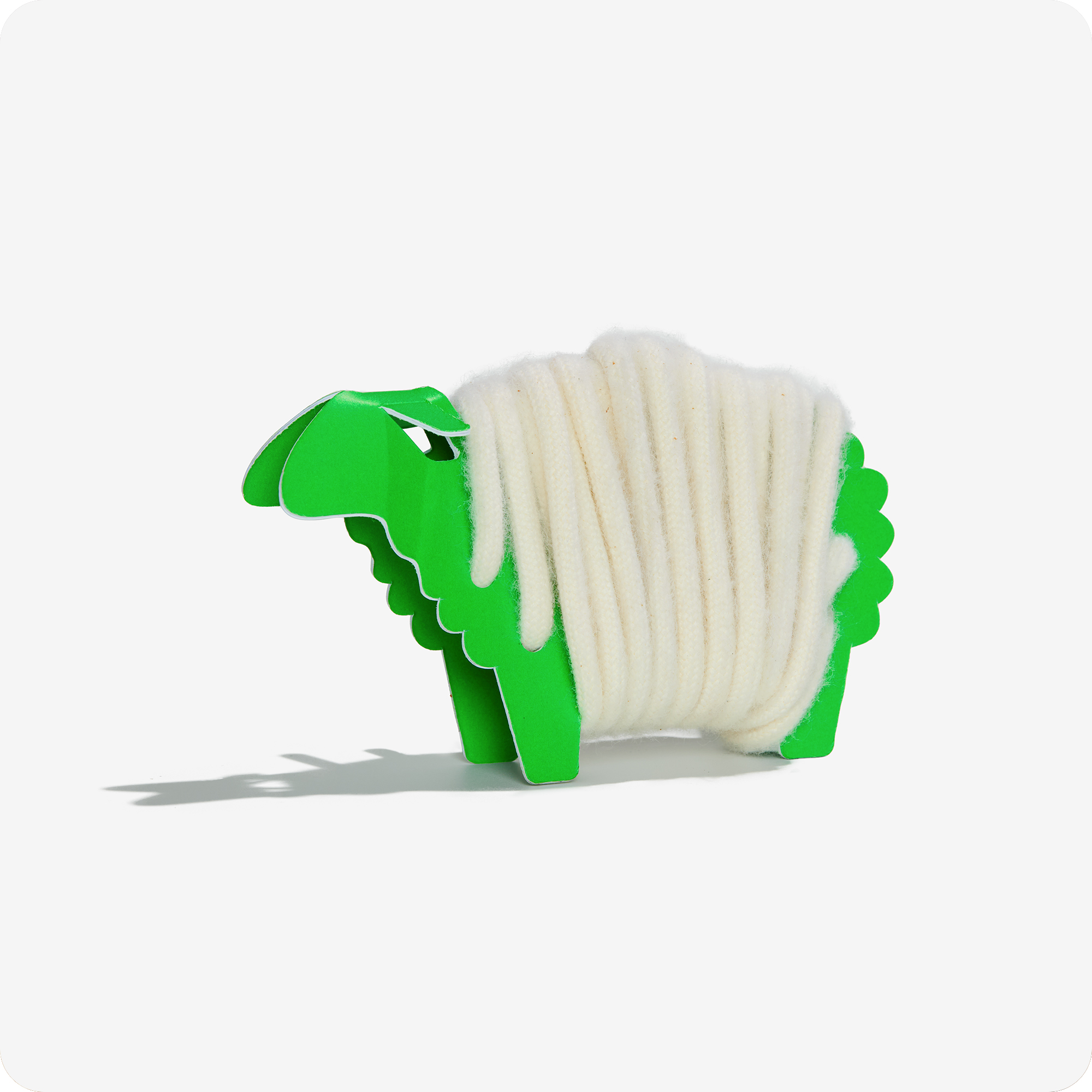 Rainbow Wool Schnürsenkel aus schwuler Schafwolle aufgewickelt um ein grünes Papierschaf vor einem weißen Hintergrund.