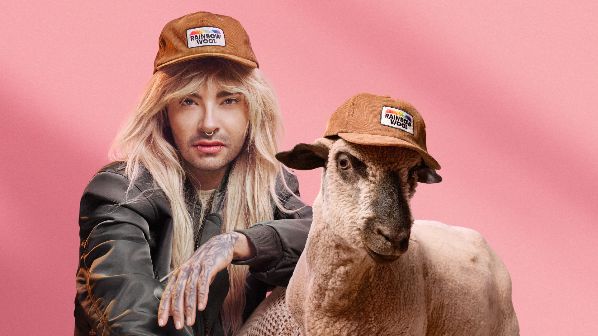 Bill Kaulitz posing next to his sponsorsheep in front if a pink background.